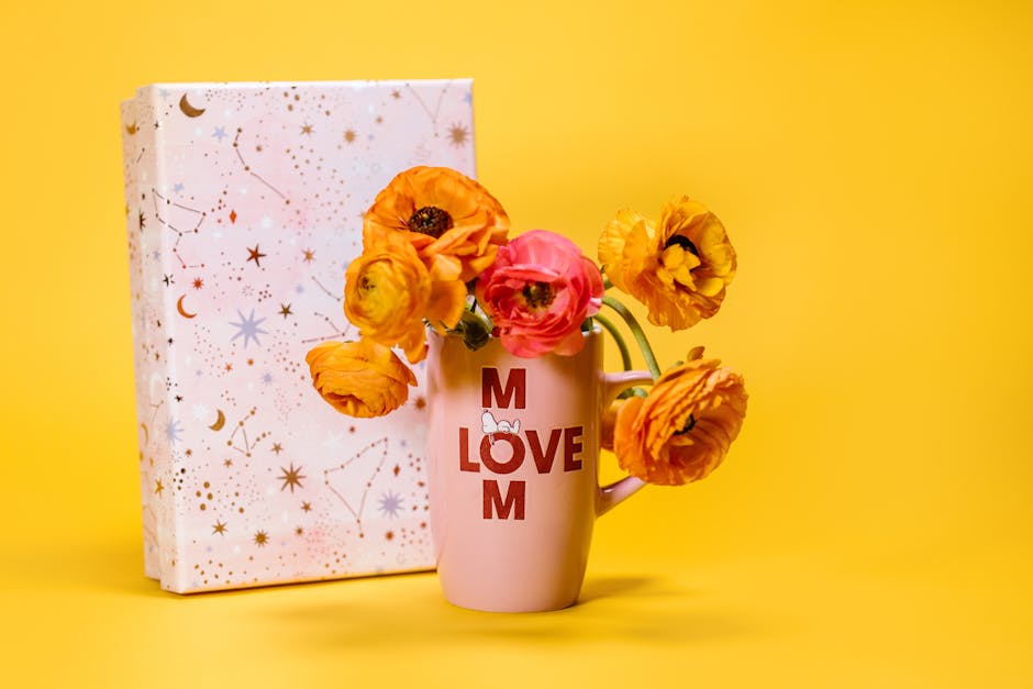 pexels-photo-7764514-7764514 Vibrant flowers in a 'Love Mom' mug with a constellation gift box on a yellow backdrop.
